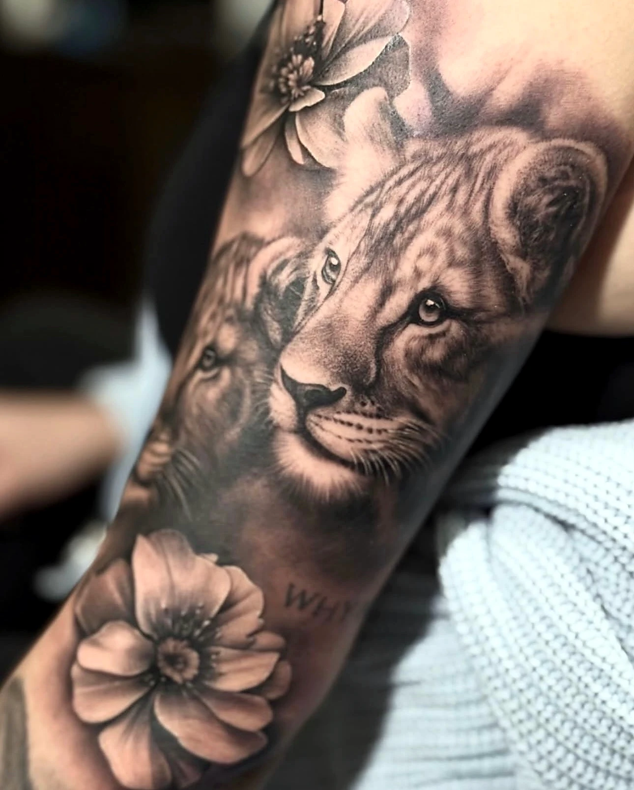 Black and grey realism lion cub with florals by Rav Singh at Inkology